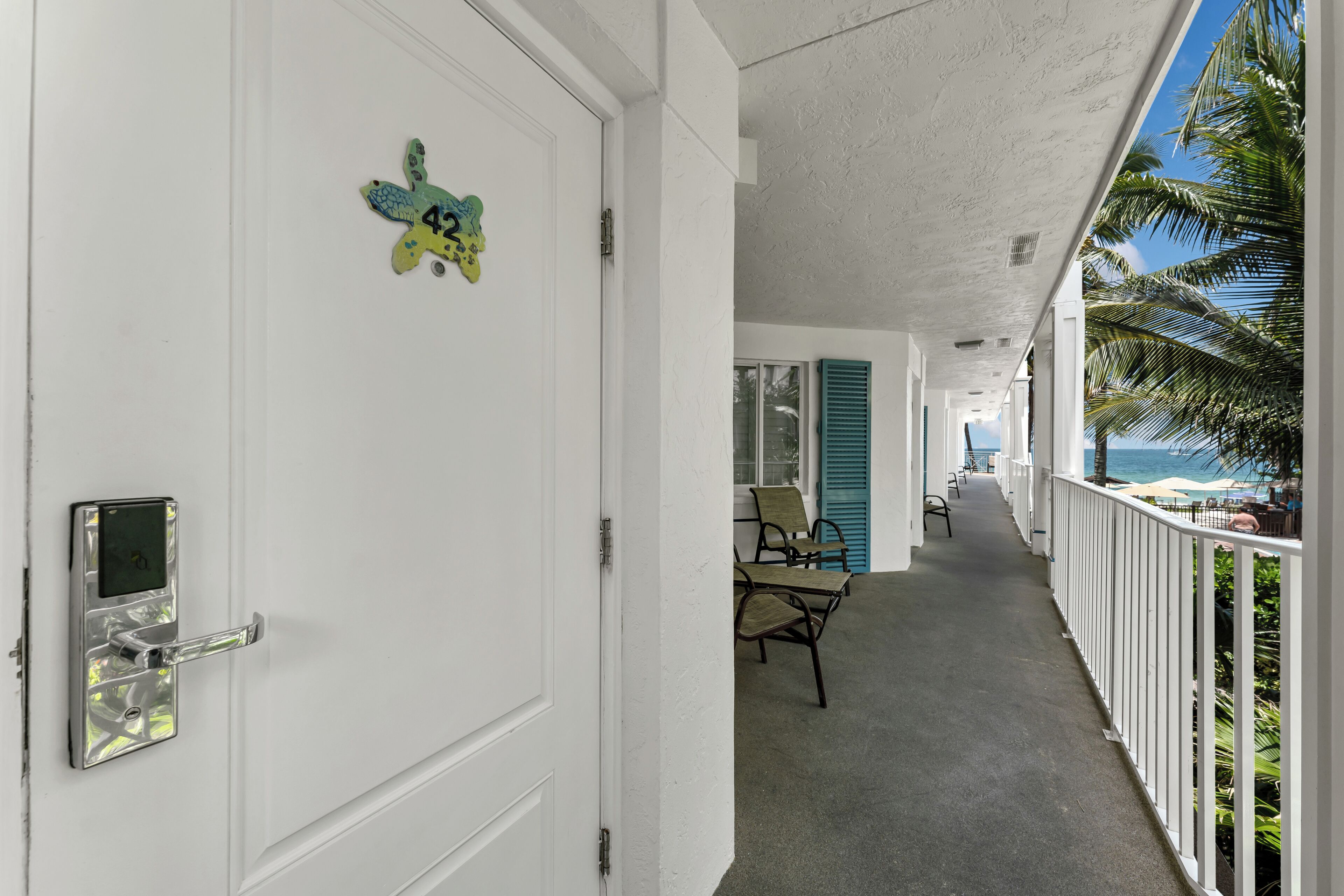 A hotel corridor with a white door, a digital lock, and a butterfly-shaped number plate.