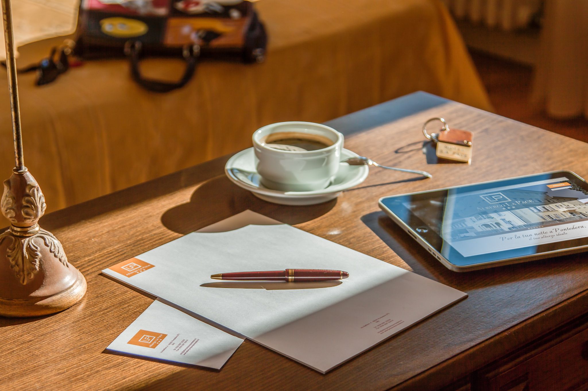 Une table en bois avec une tasse de café, un stylo, des papiers, une tablette et un petit porte-clés.