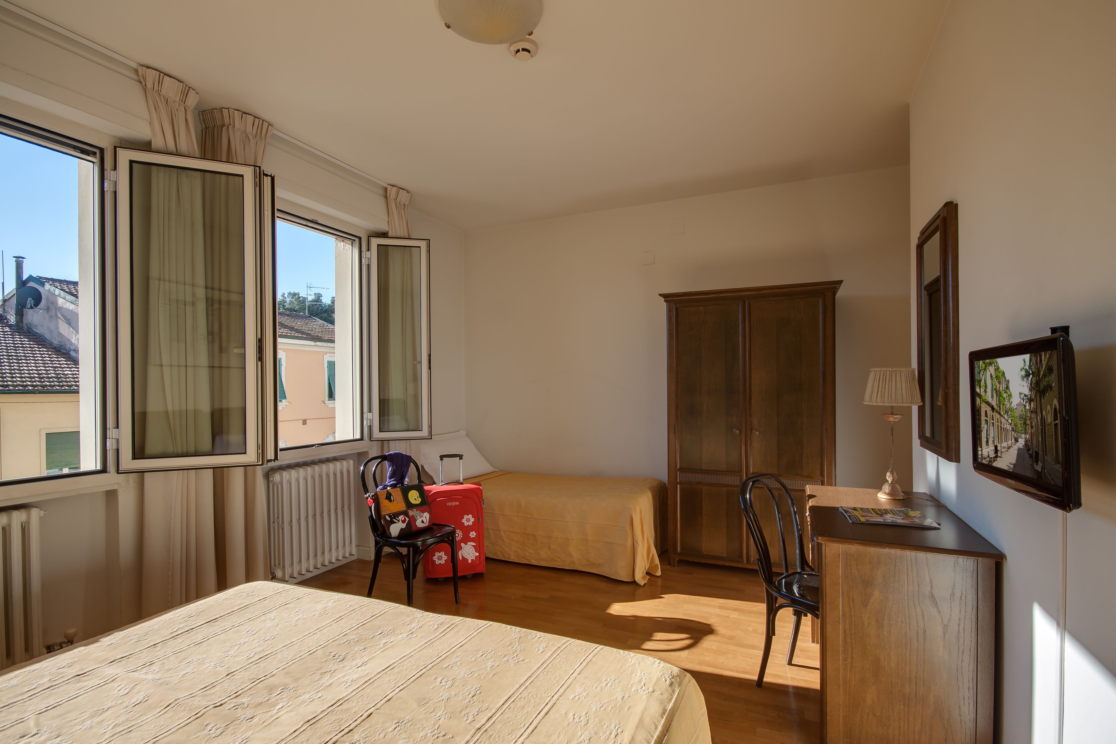 A bedroom with a bed, a desk, a chair, a wardrobe, and a window with curtains.