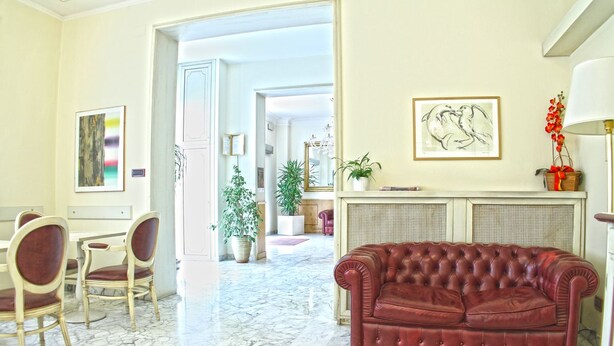 A spacious living room with a red leather sofa, marble flooring, and a dining area with chairs and a table. - Hotel La Pace (Pontedera)