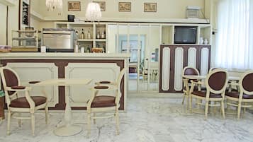 Un espace repas doté d’un sol en marbre, un bar avec un comptoir et un téléviseur posé sur un meuble.