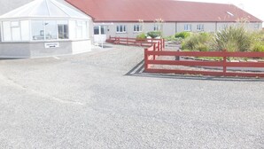 A building with a red roof, a covered area with windows, and a gravel driveway. - Orkneylodge (Orphir)