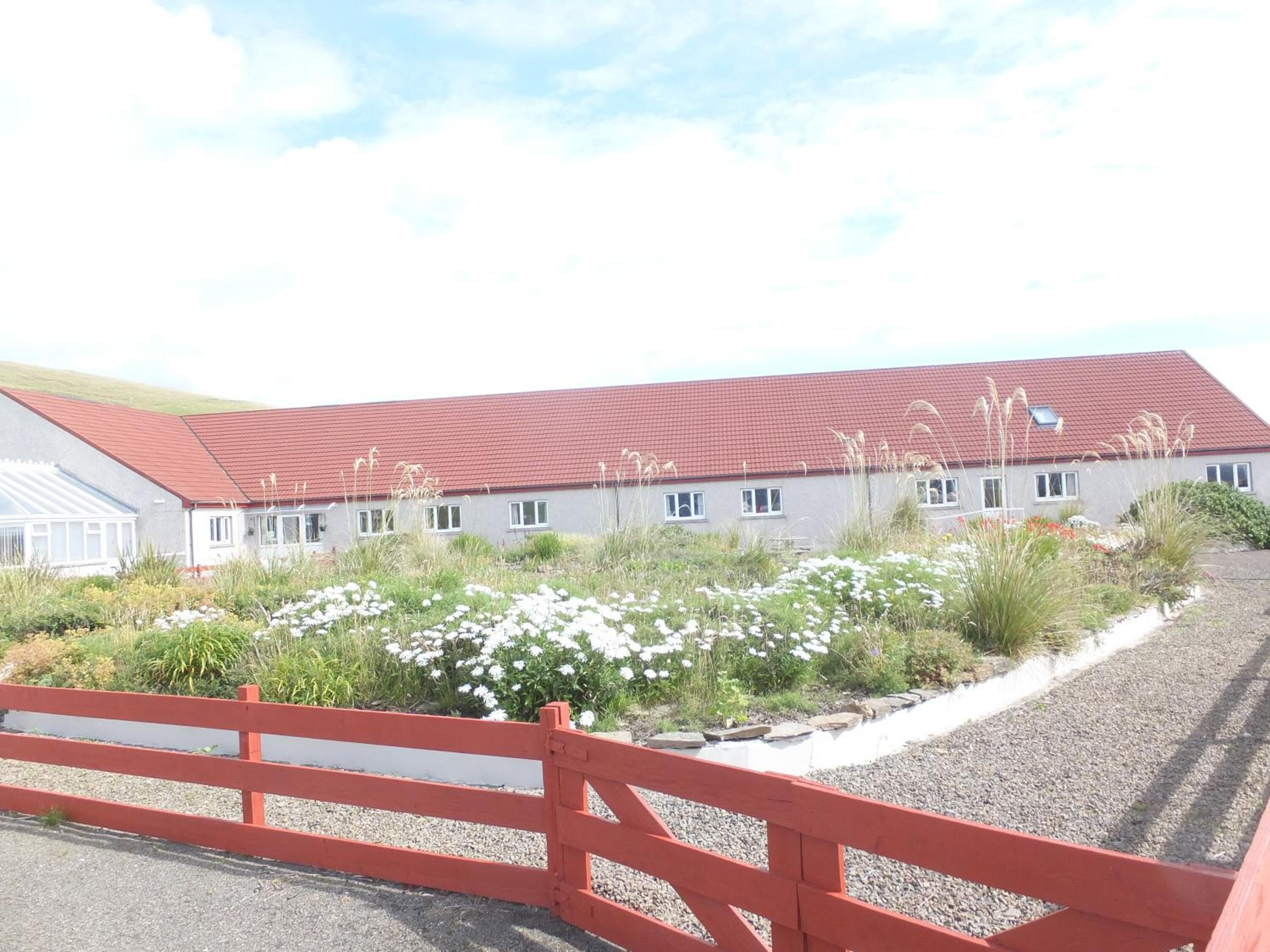 A building with a red roof, surrounded by a gravel driveway and a red fence.