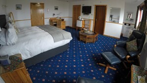 A hotel room with a bed, a desk, a chair, a television, and a small kitchenette. - Orkneylodge (Orphir)