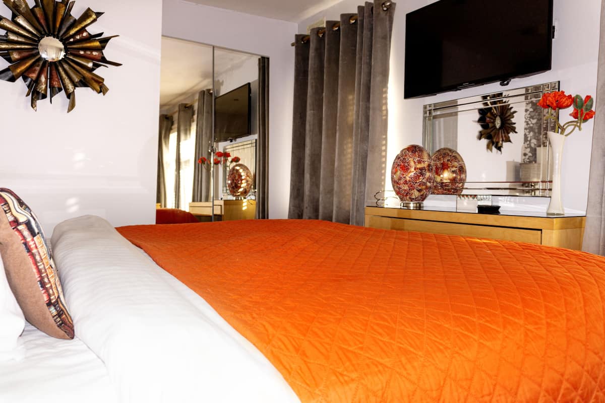 A bedroom with a large bed, a dresser, a mirror, and a television on the wall.