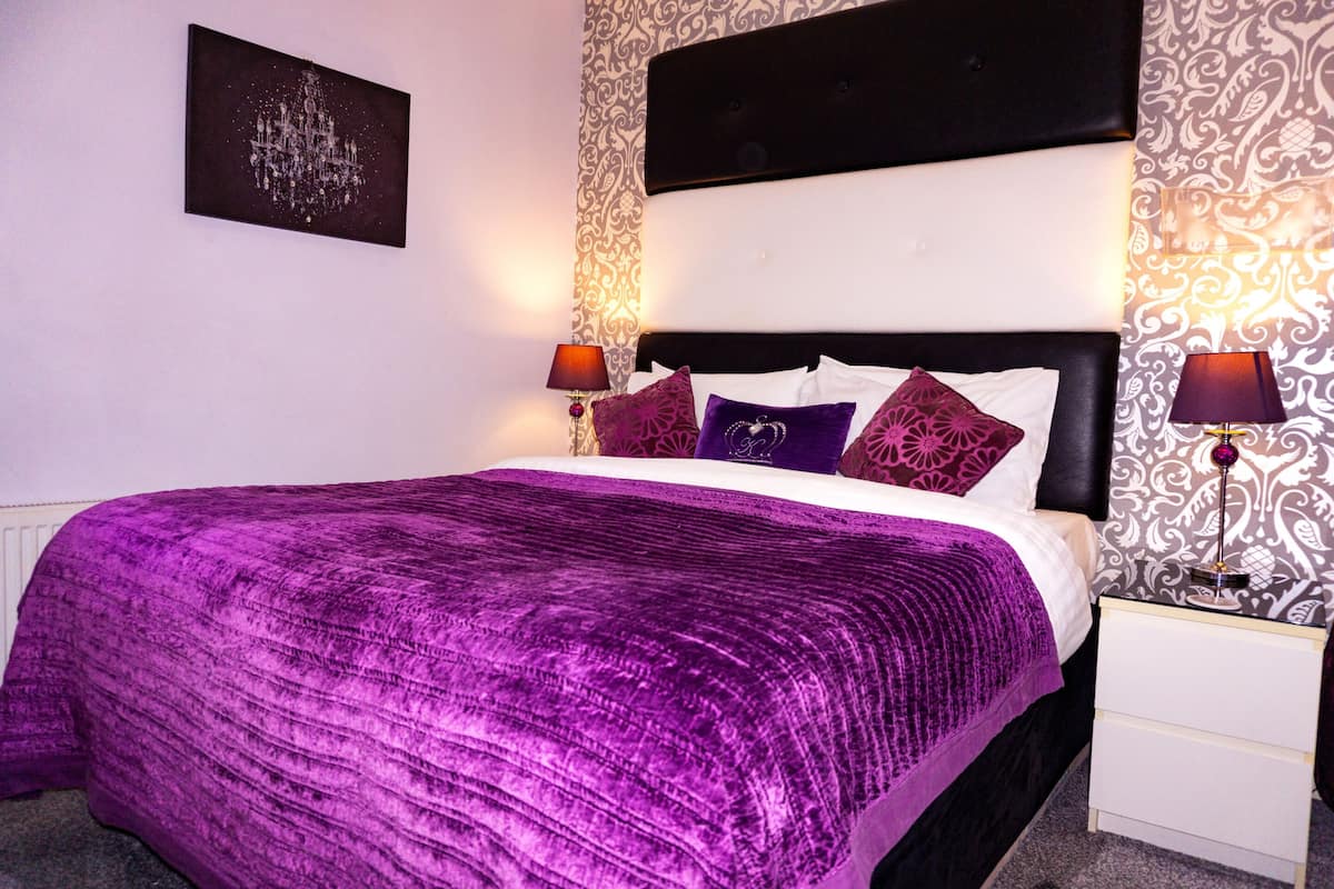 A neatly made bed with a purple bedspread, a black headboard, and two bedside lamps.