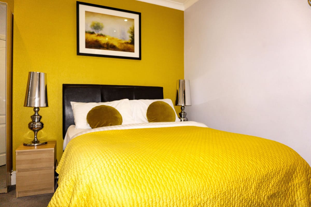 A bed with a yellow bedspread, two bedside lamps, and a framed picture on the wall.