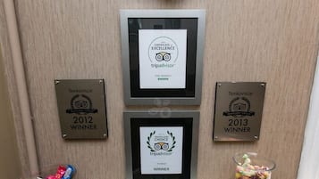 Three framed TripAdvisor awards on a wall, a glass candy dish, and a small pile of assorted candies.