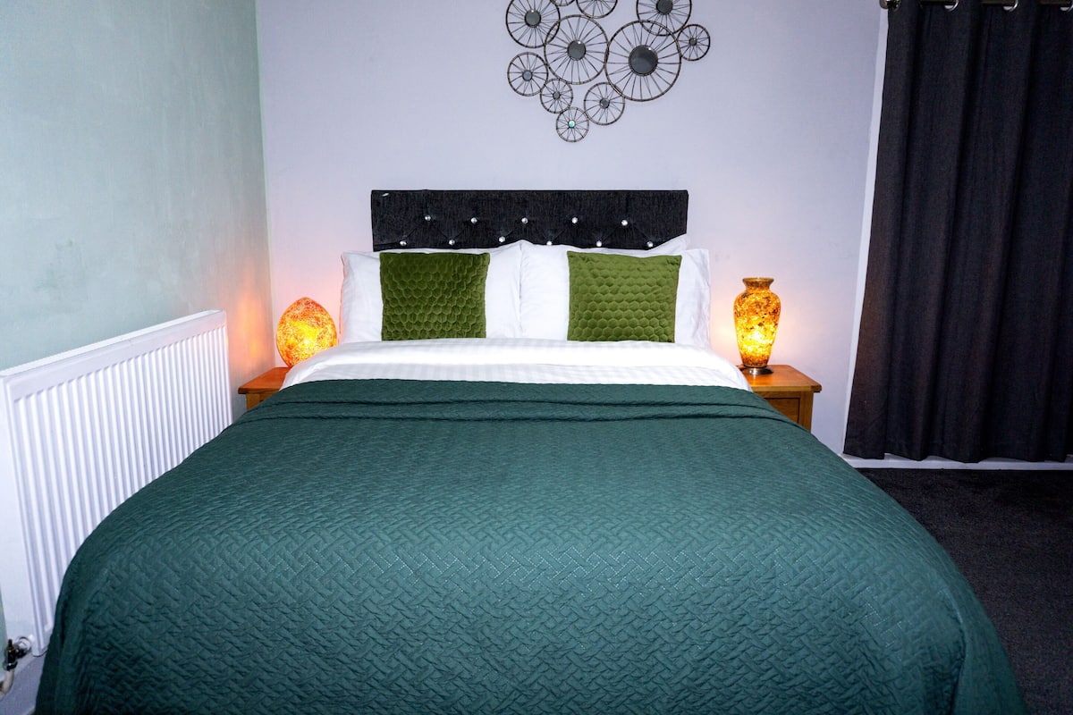 A neatly made bed with a green quilt, white pillows, and a decorative headboard.