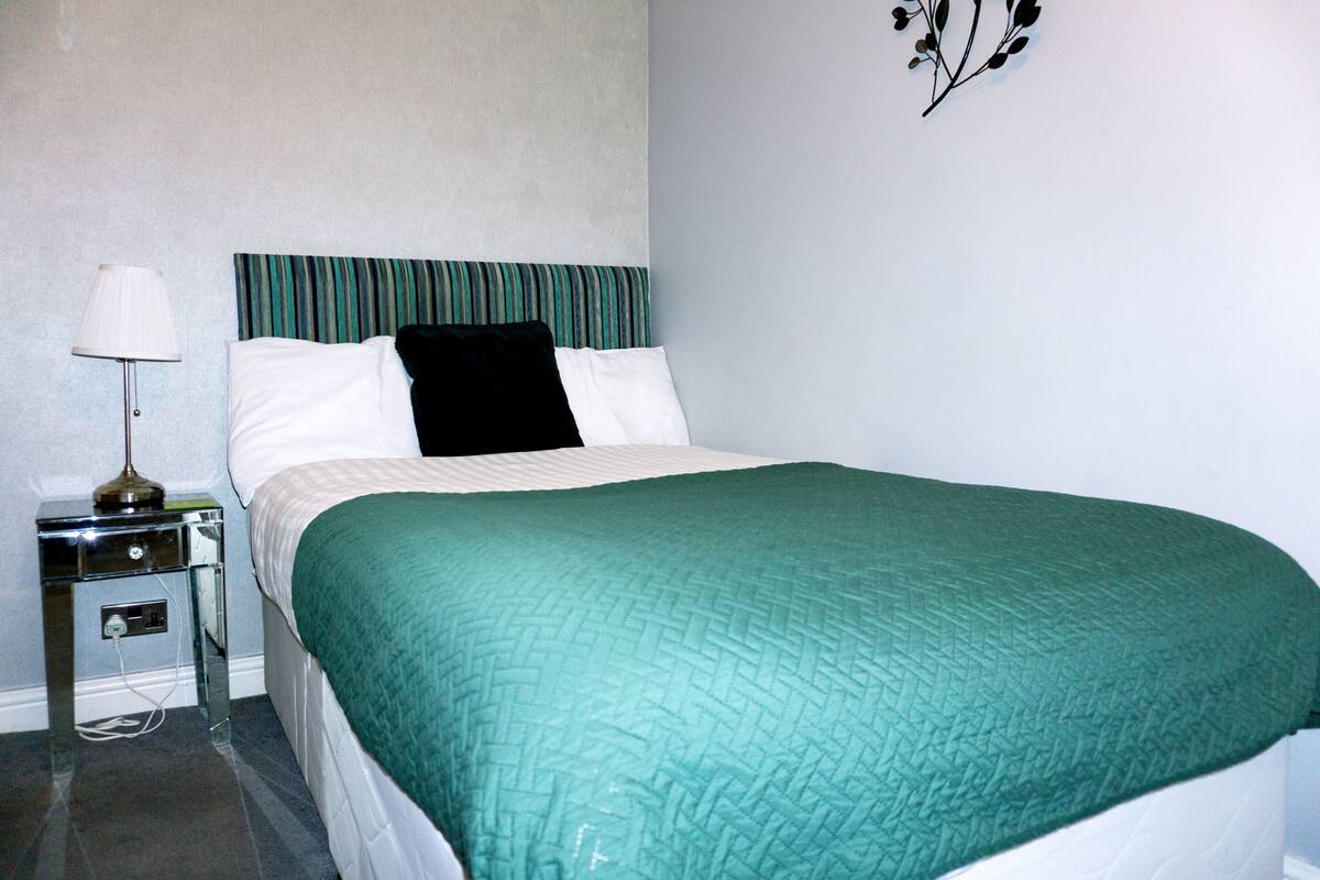 A neatly made bed with a green quilt, a black pillow, and a striped headboard.