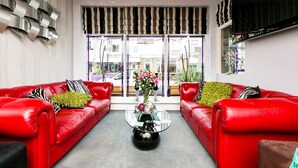 Un salon moderne avec deux canapés en cuir rouge, une table basse en verre et une grande fenêtre ornée de rideaux à rayures.