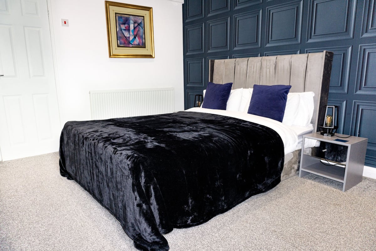 A bedroom with a large bed, a nightstand, a framed picture on the wall, and a blue accent wall.