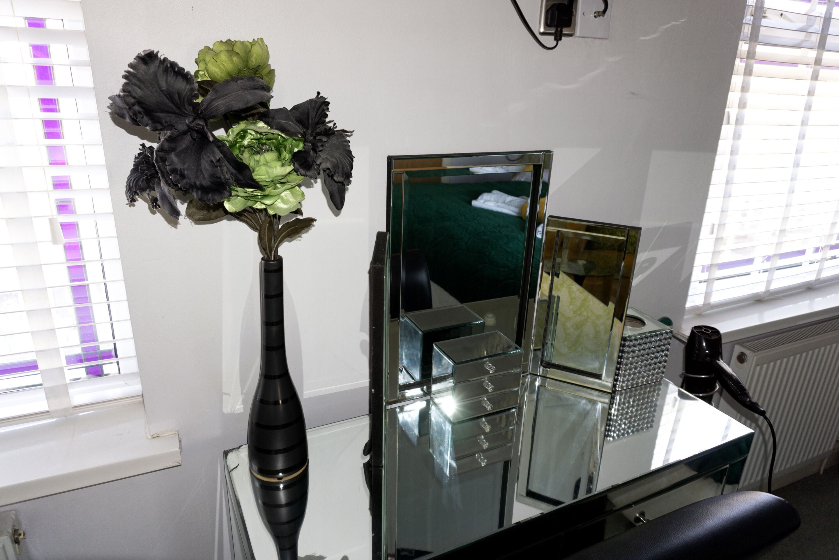 A room with a mirror, a vase with flowers, and a radiator.