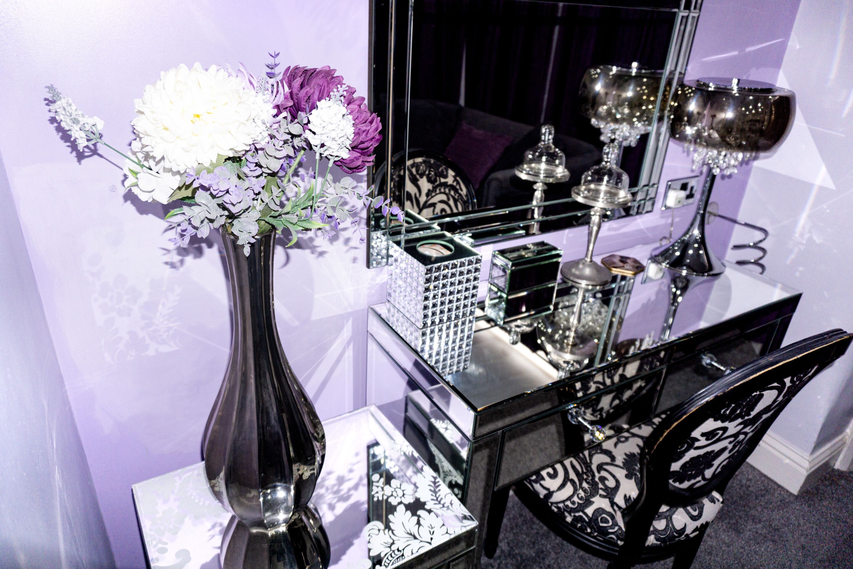 A mirror reflecting a table with a vase of flowers, a decorative box, and a candle holder.