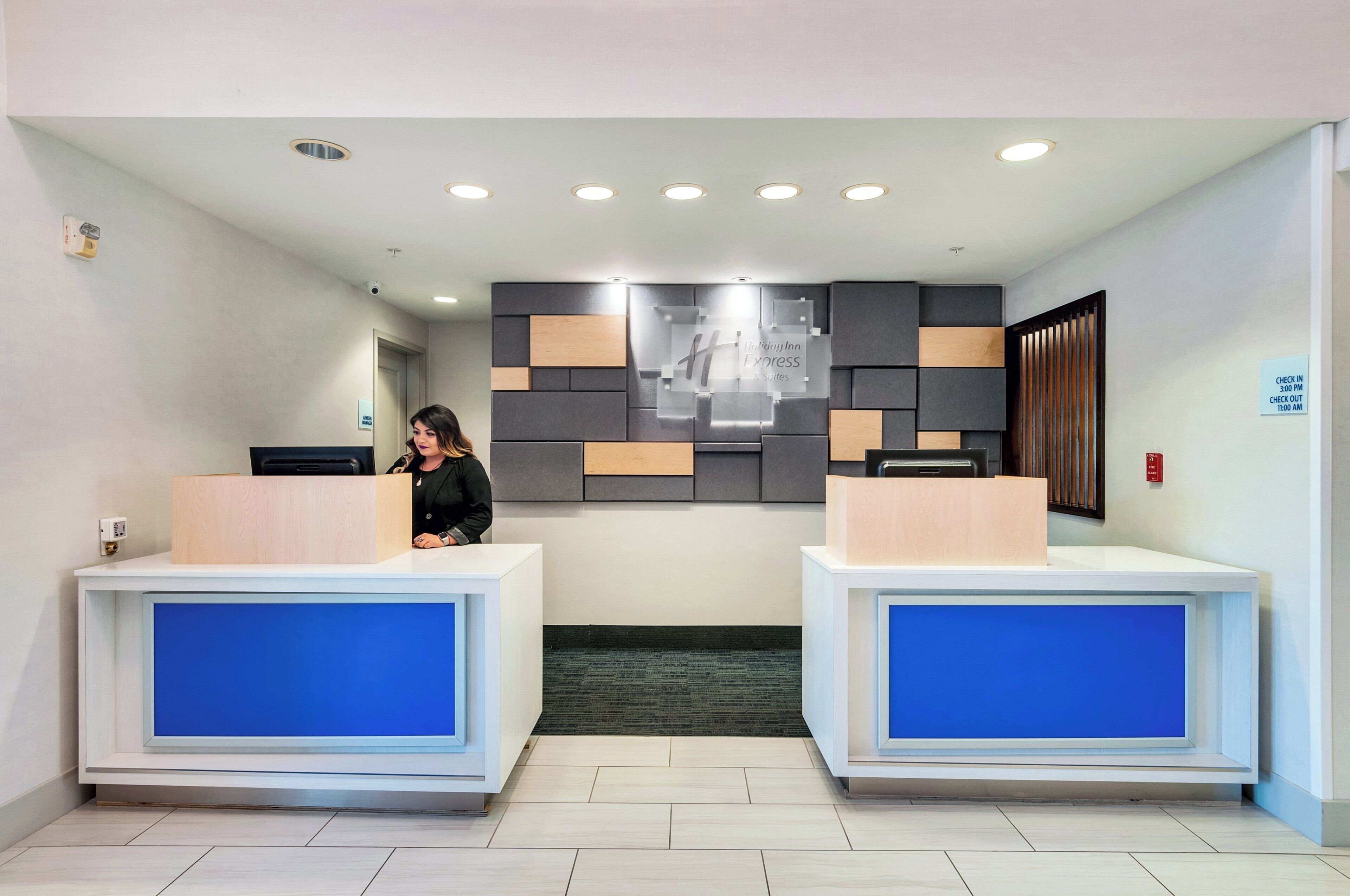 A hotel reception area with two reception desks, a wall-mounted sign, and a security camera.