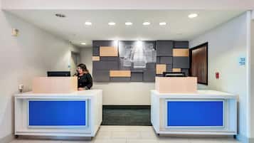 A hotel reception area with two reception desks, a wall-mounted sign, and a security camera.