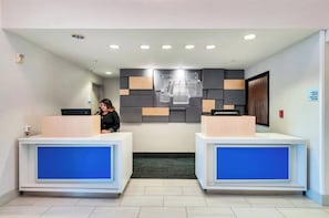 Área de recepção de hotel com dois balcões, uma placa na parede e uma câmera de segurança.