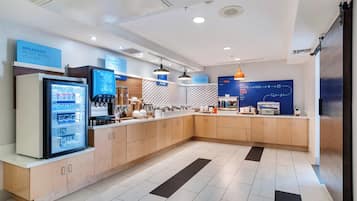 Una cocina moderna con refrigerador, cafetera y un letrero azul que indica opciones de desayuno.