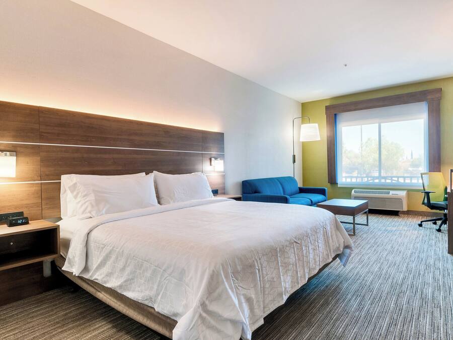 A hotel room with a large bed, bedside tables, a desk, a chair, and a window with a view.
