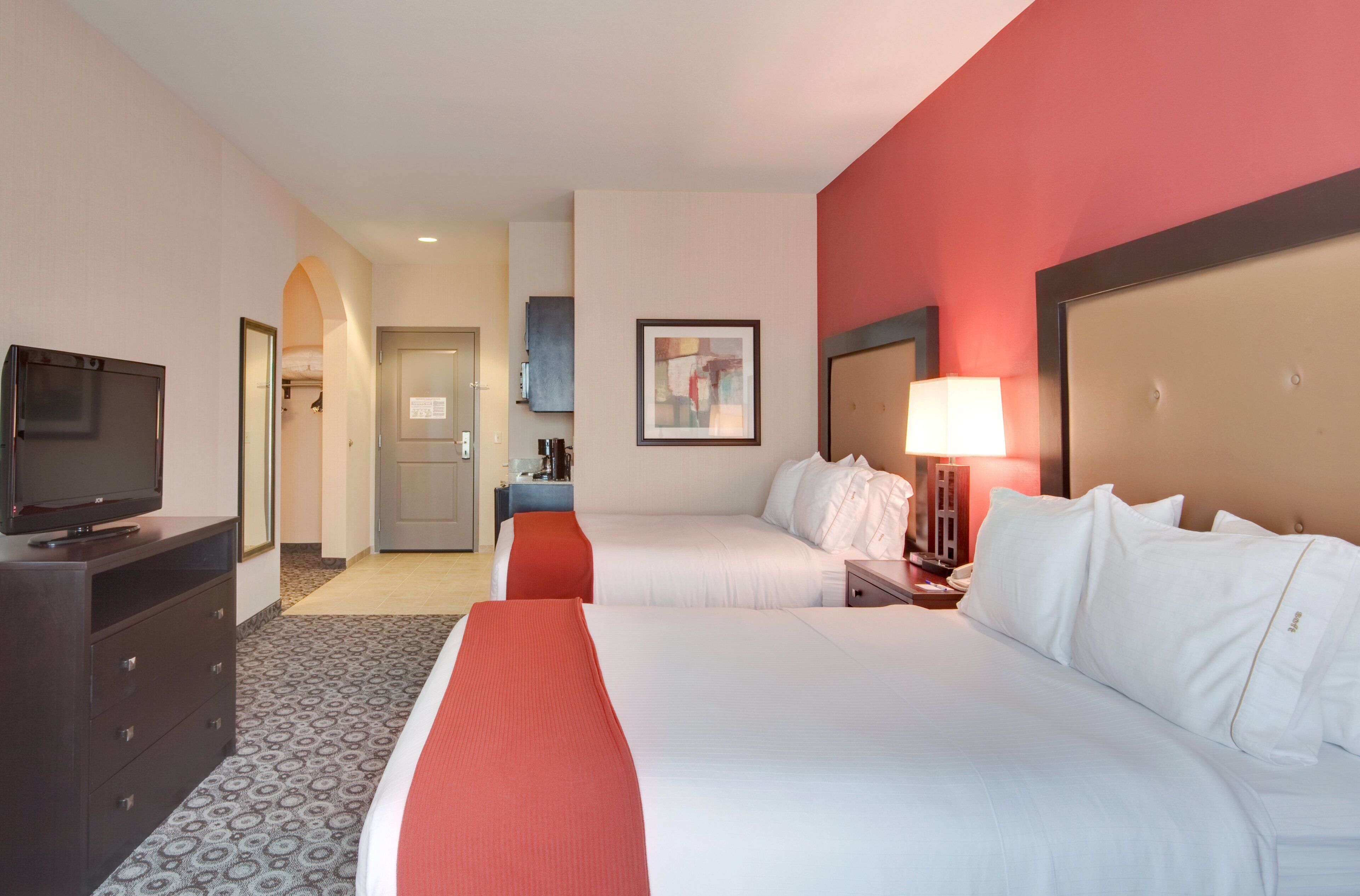 A hotel room with two beds, a television, a desk, and a painting on the wall.