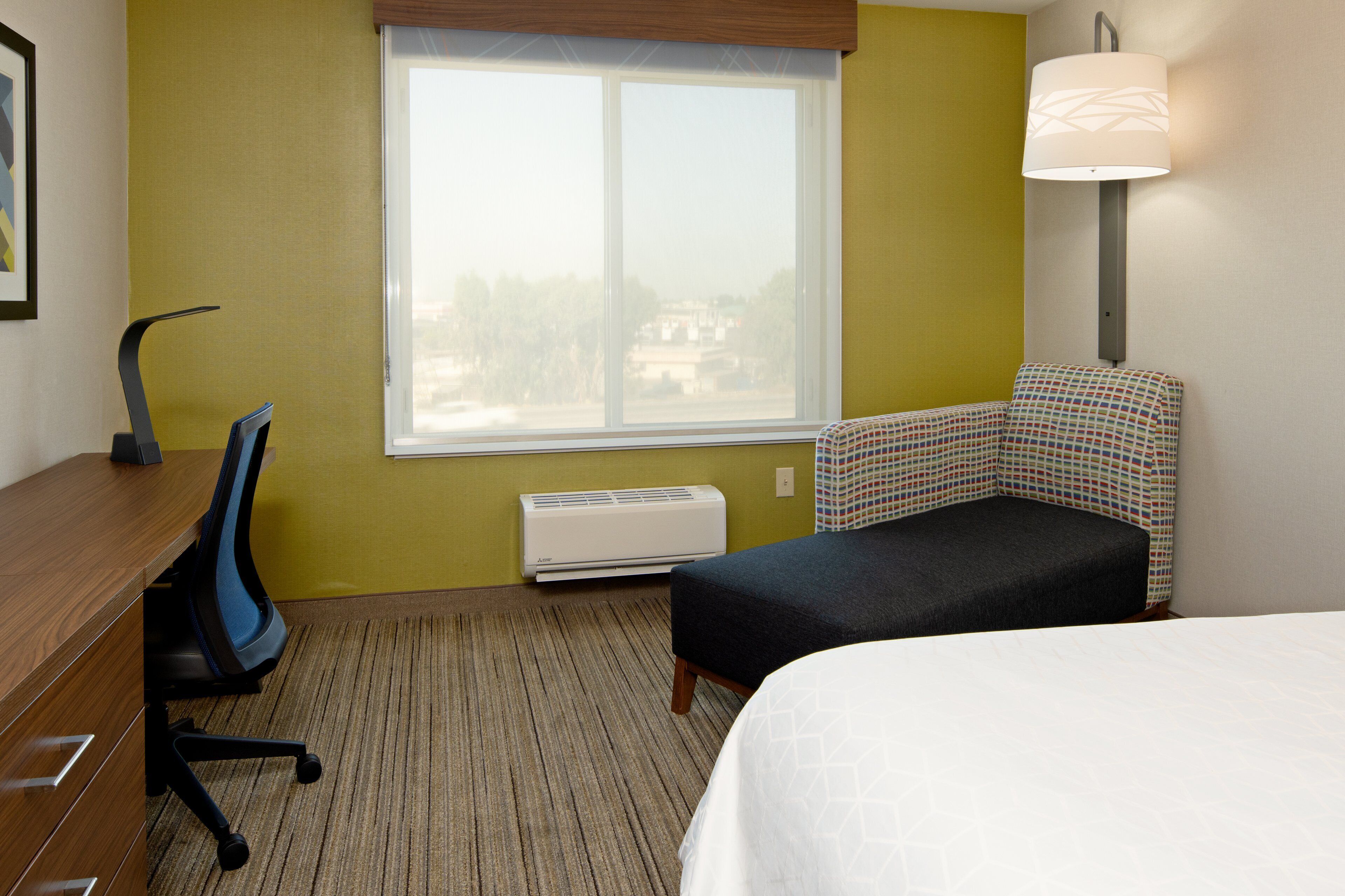 Ein Hotelzimmer mit Bett, Schreibtisch mit Stuhl, Fenster mit Blick und einer Wandlampe.