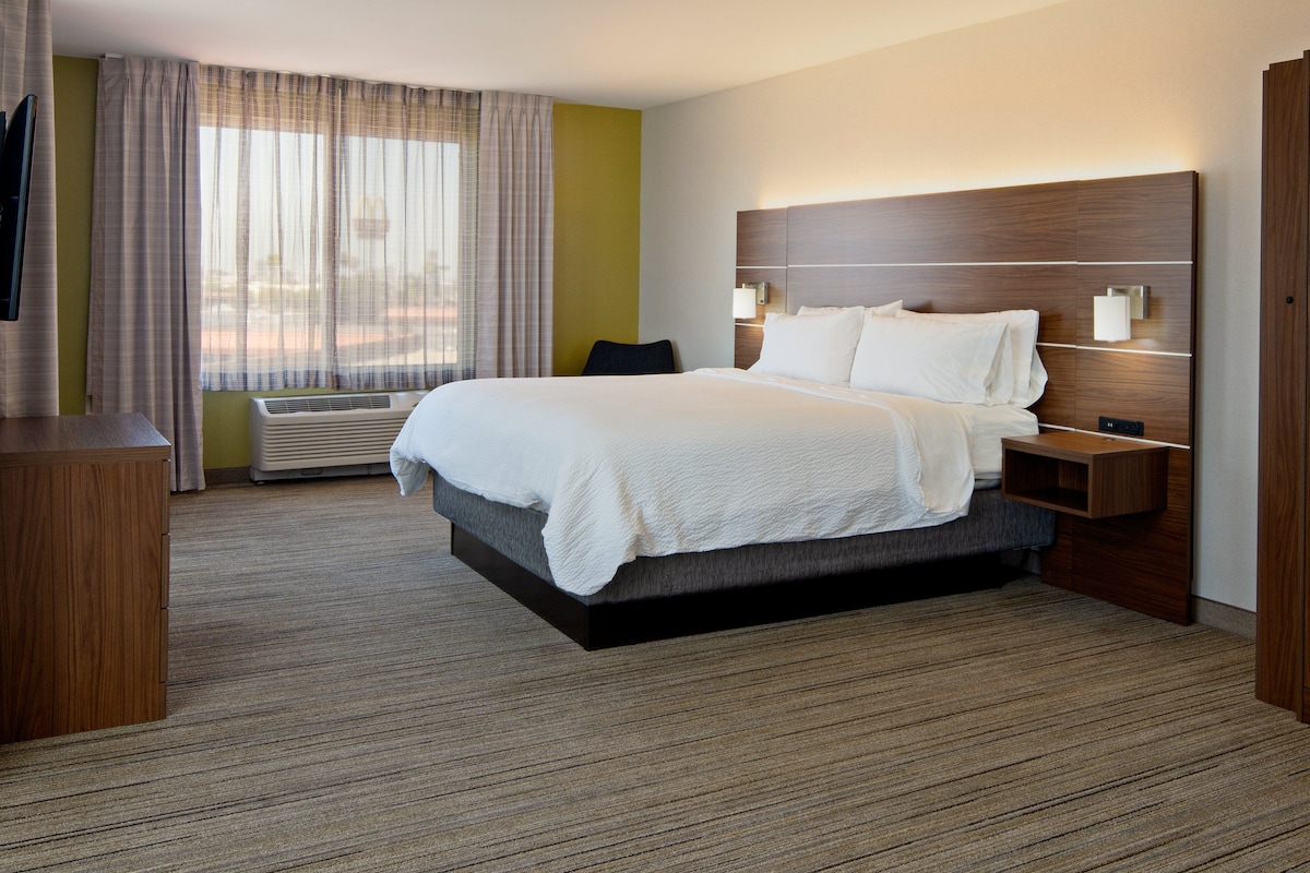 A hotel room with a large bed, bedside tables, a TV, a desk, and a window with curtains.