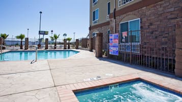 A hotel swimming pool area with a hot tub, a fenced pool, and a building with a brick facade.