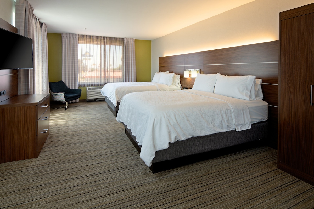 A hotel room with two beds, a TV, a chair, and a desk.