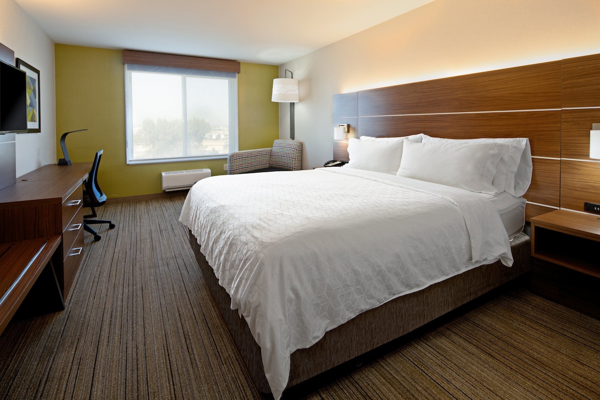 A hotel room with a large bed, a desk, a chair, a TV, and a window.