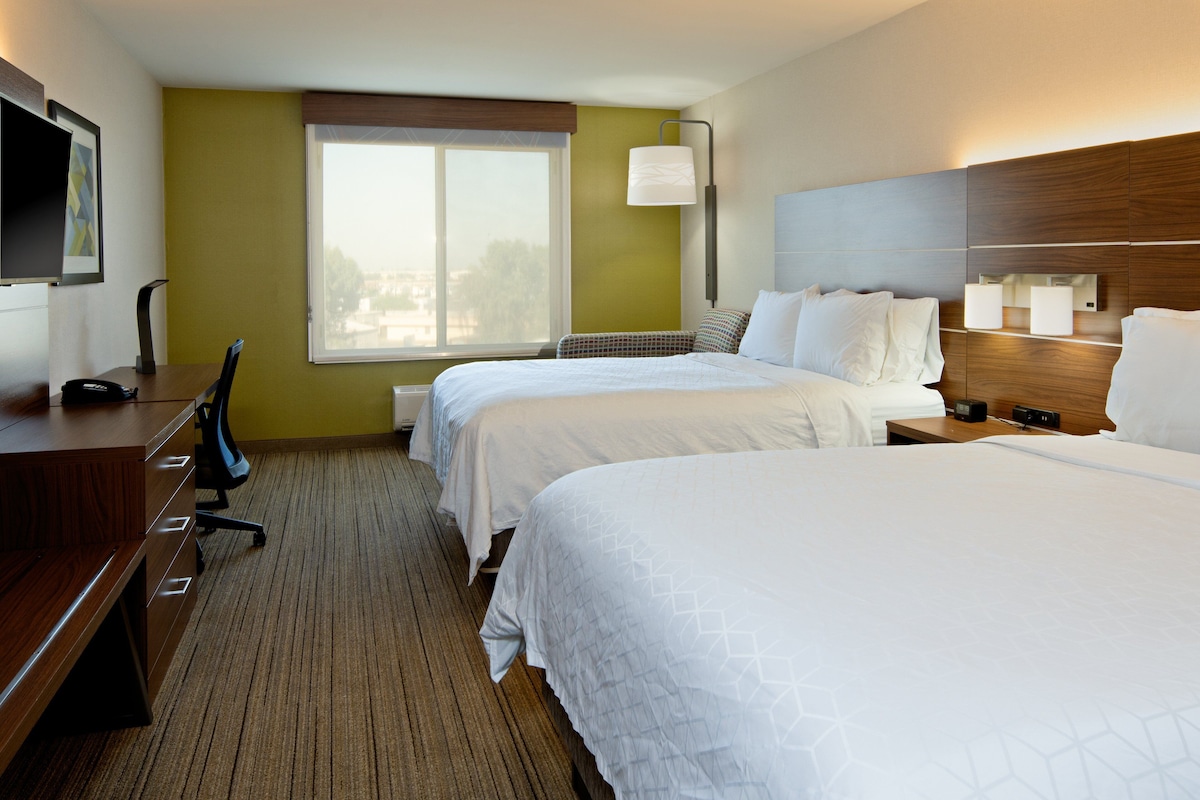 A hotel room with two beds, a desk, a chair, and a television.