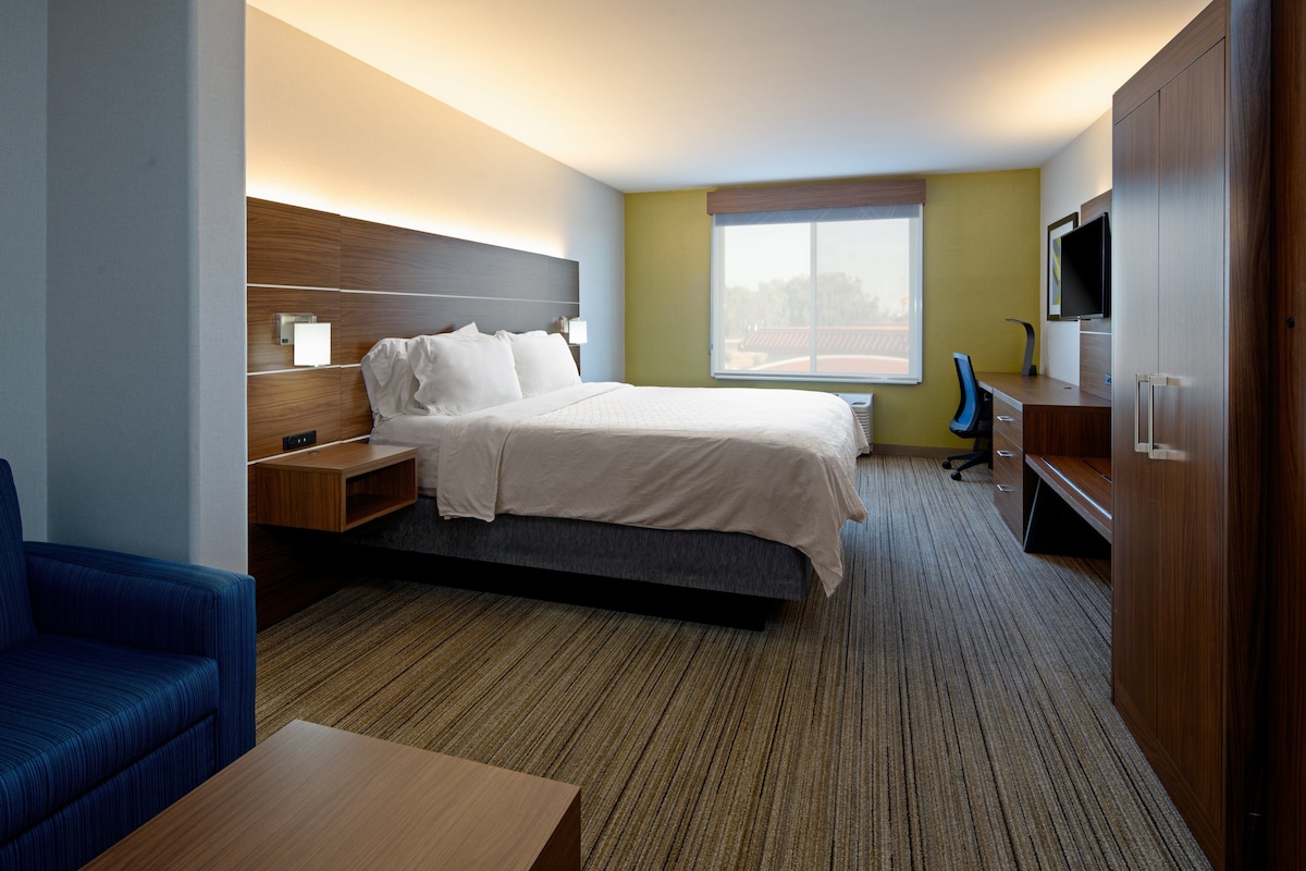 A hotel room with a bed, a desk, a chair, a television, and a window.