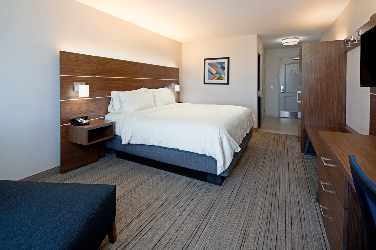 A modern hotel room with a large bed, bedside tables, a desk, and a television.