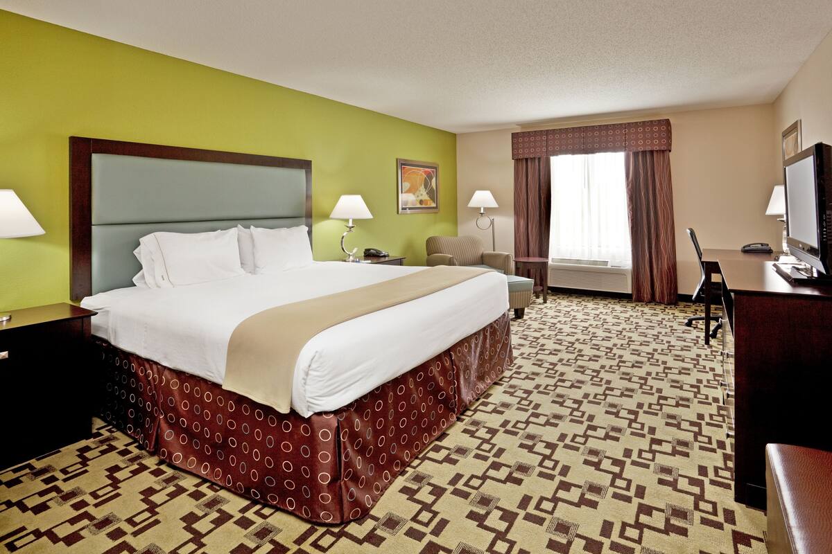 Ein Hotelzimmer mit einem großen Bett, zwei Nachttischen, einem Schreibtisch, einem Sessel und einem Fernseher.