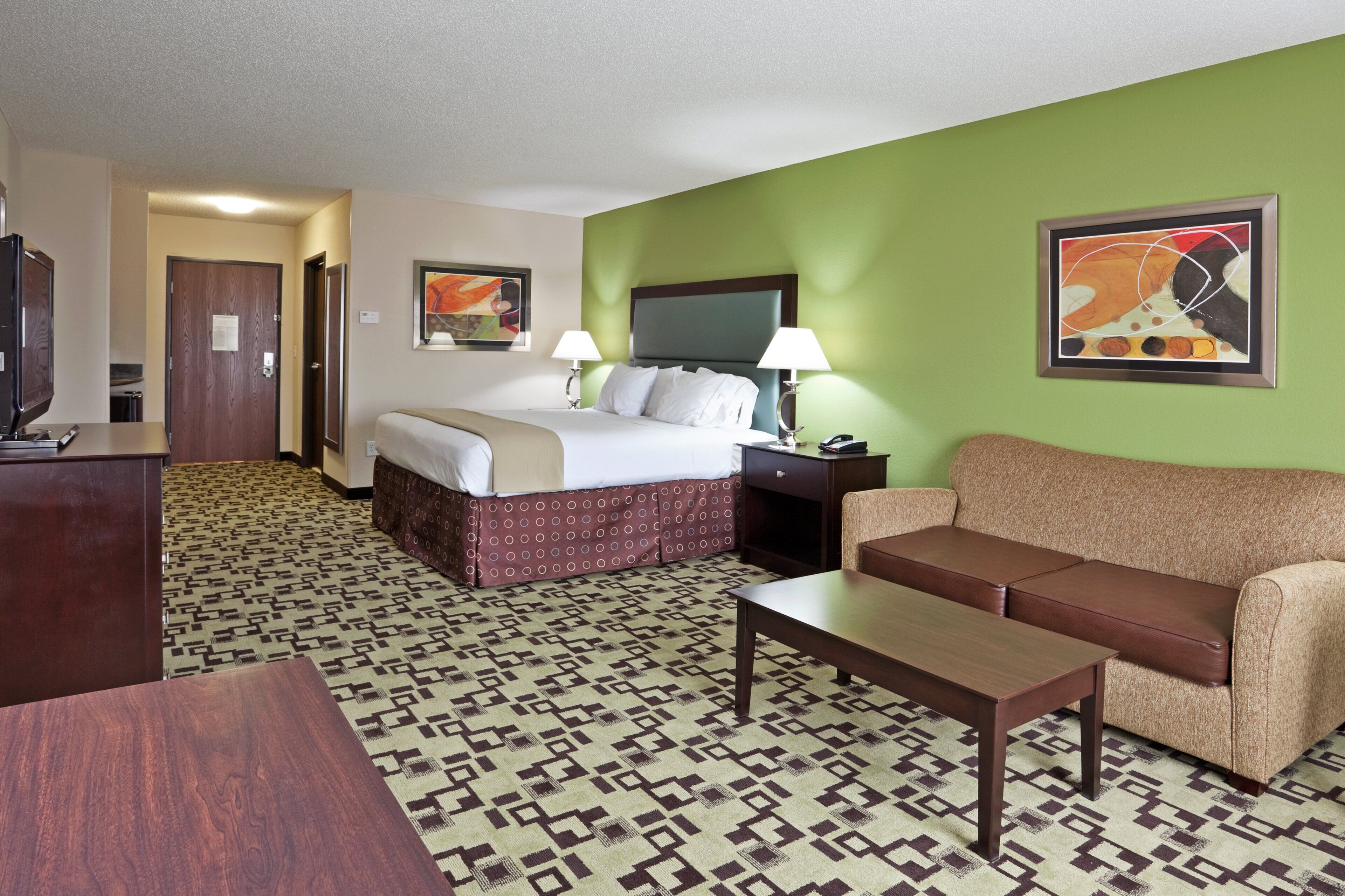 A hotel room with a bed, a sofa, a desk, and a television.