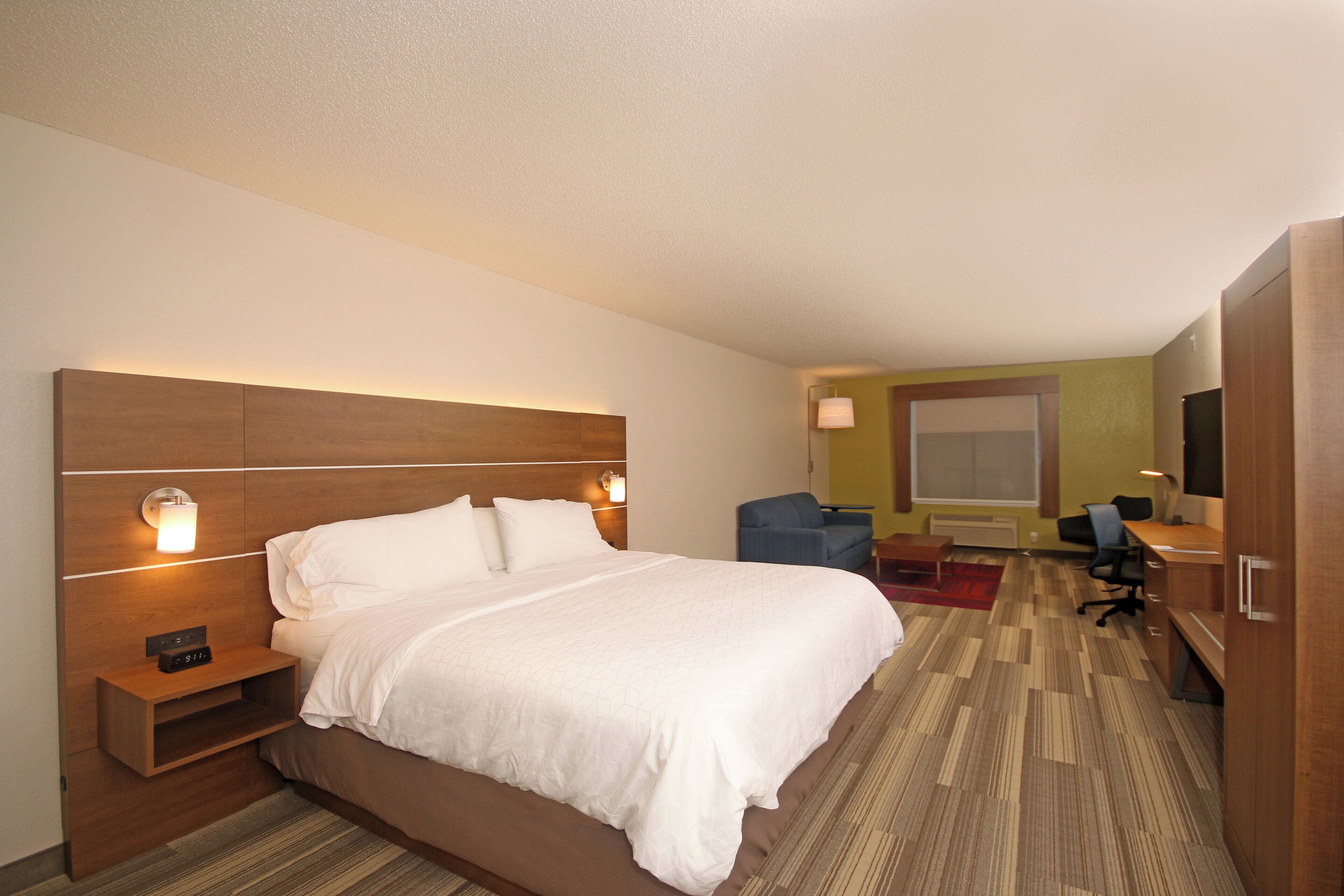 A hotel room with a large bed, bedside tables, a desk, a chair, a TV, and a window.