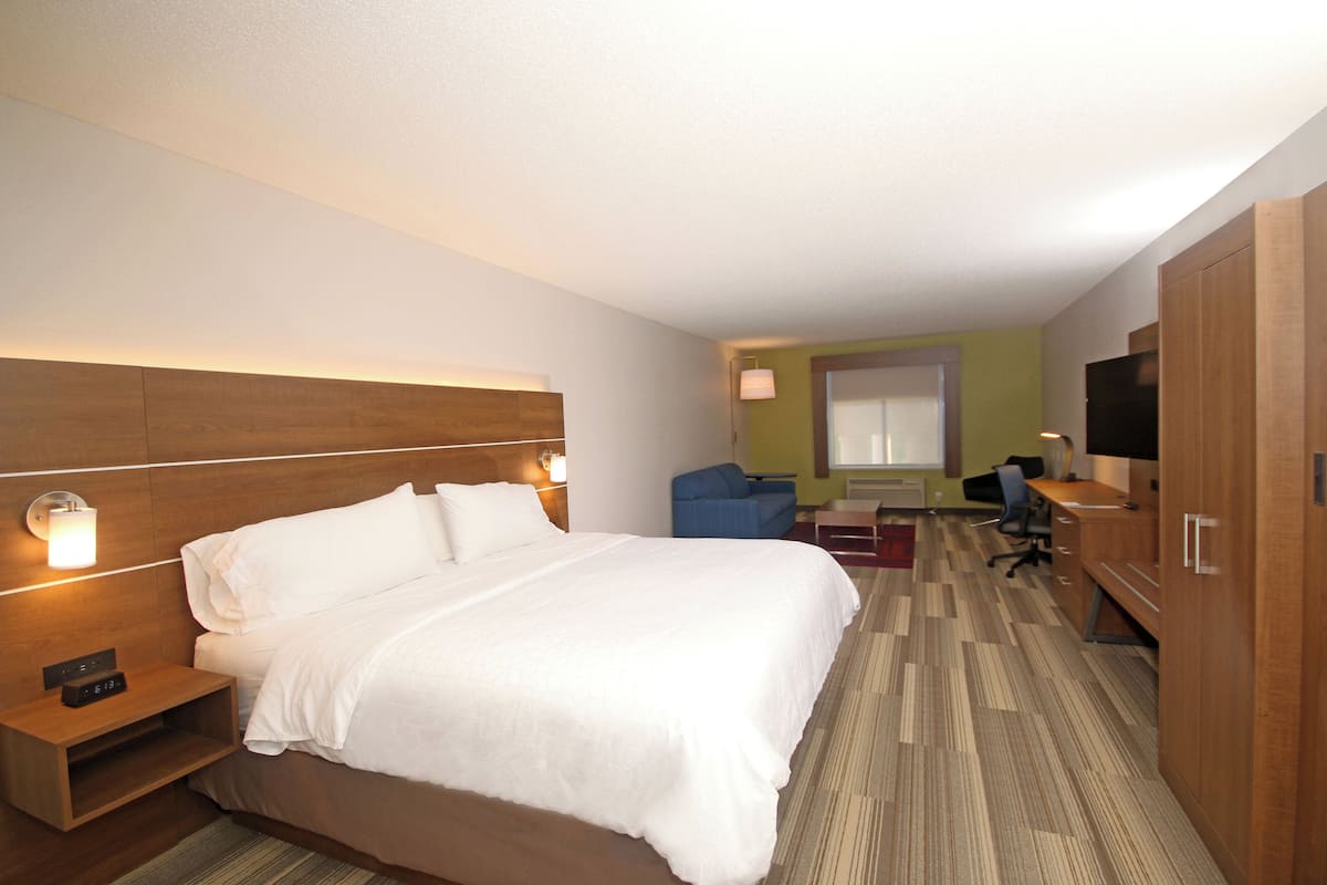 Ein Hotelzimmer mit einem großen Bett, einem Schreibtisch, einem Sessel, einem Fernseher und einem Fenster.