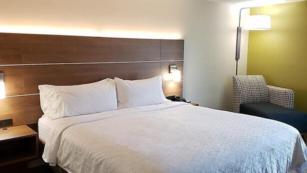 Hotellihuone, jossa on suuri sänky, yöpöydällä olevat lamput, yöpöytä ja tuoli.