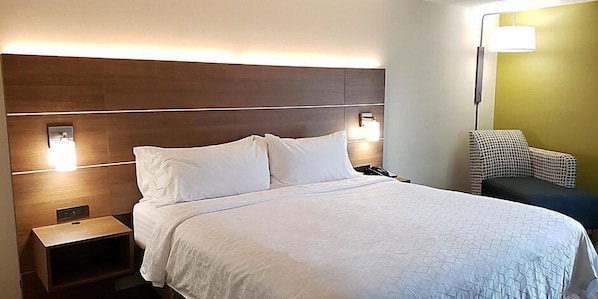 Quarto de hotel com uma cama grande, abajures, mesa de cabeceira e uma cadeira.