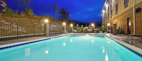A swimming pool with a metal fence, a brick building, and a clear sky.