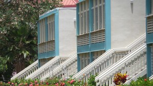 A row of two-story buildings with white railings and a garden with red and purple flowers in front. - Crystal Cove Villas (St. Thomas)