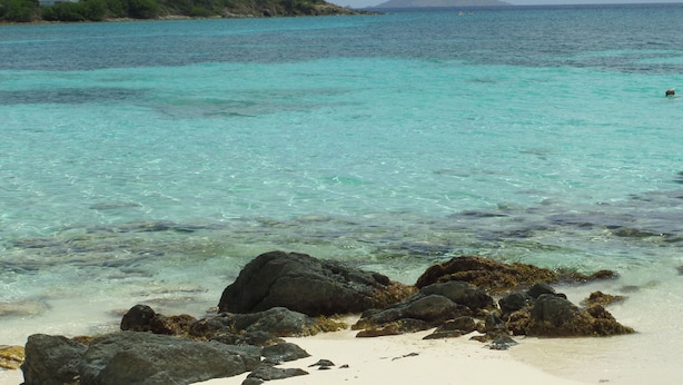 A beach with clear turquoise water, rocky shoreline, and a distant mountain. - Crystal Cove Villas (St. Thomas)