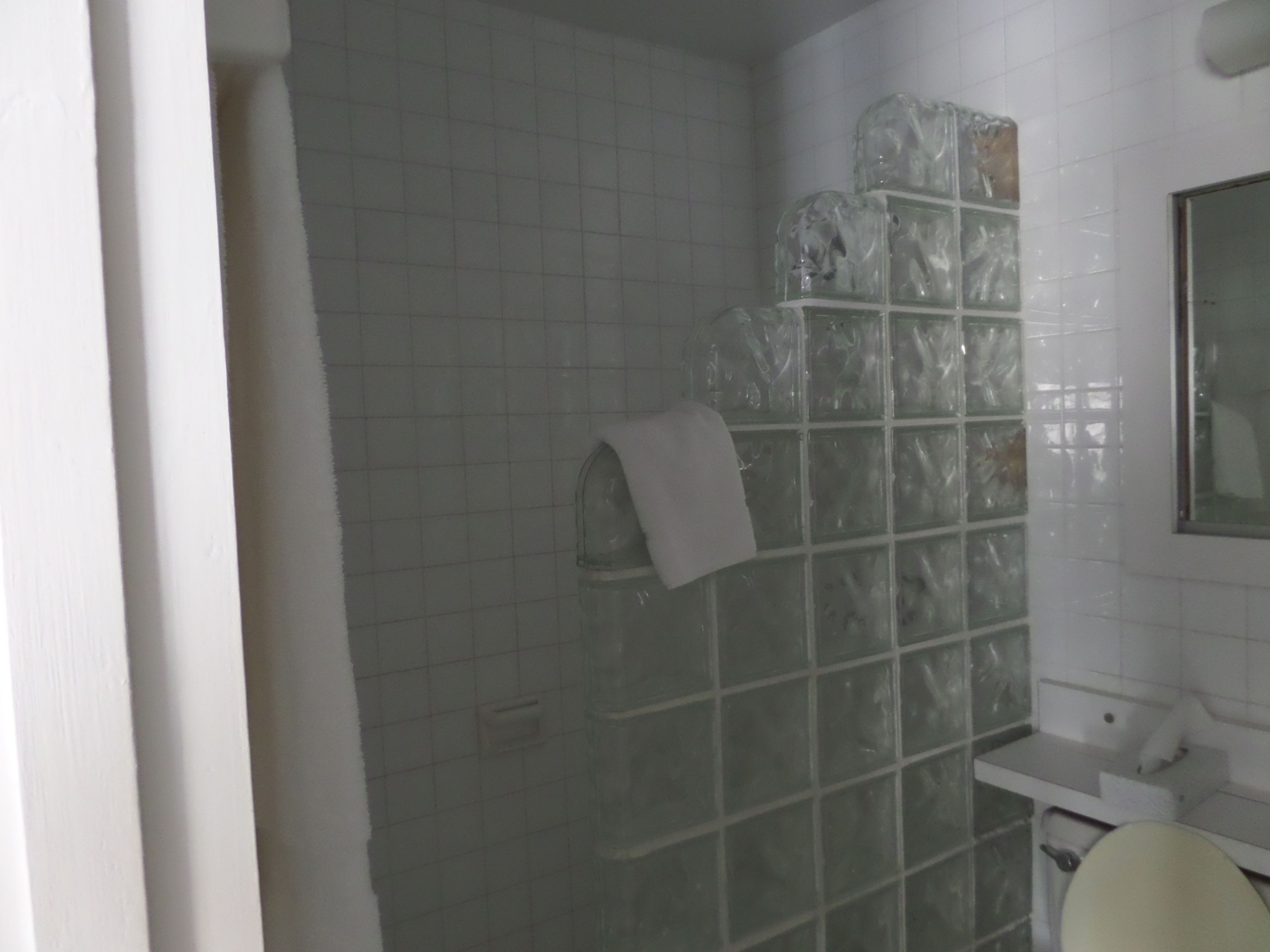 A bathroom with white tiled walls, a glass shower enclosure, a white sink, and a mirror.