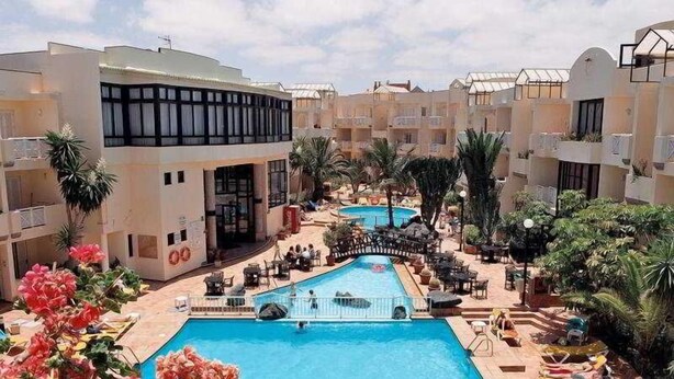 A pool area with two swimming pools, lounge chairs, and palm trees. - Fresh Corralejo Garden (La Oliva)