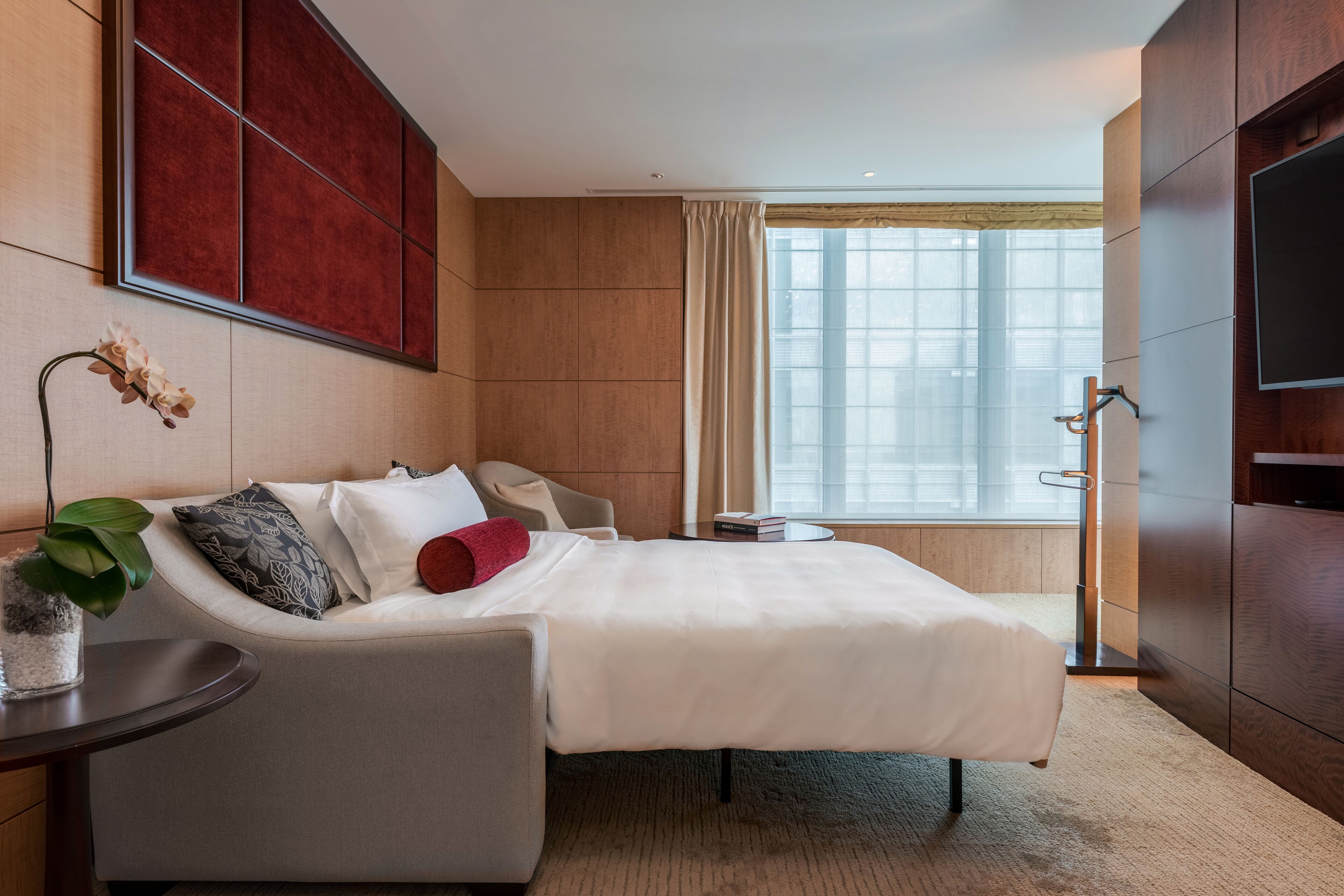 Een hotelkamer met een bed, een zithoek, een televisie en een raam met gordijnen.