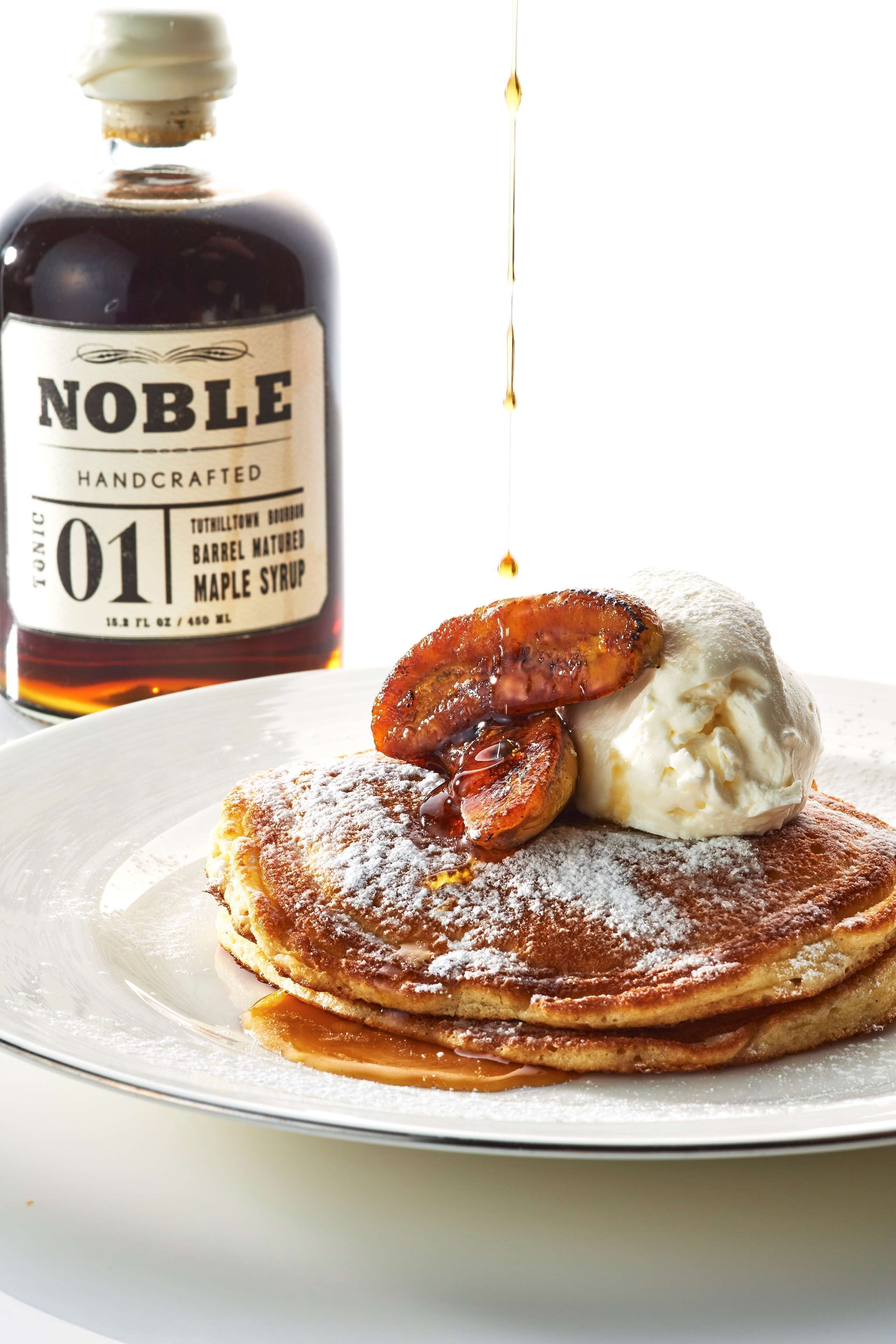 A stack of pancakes with a maple syrup bottle and a scoop of ice cream.