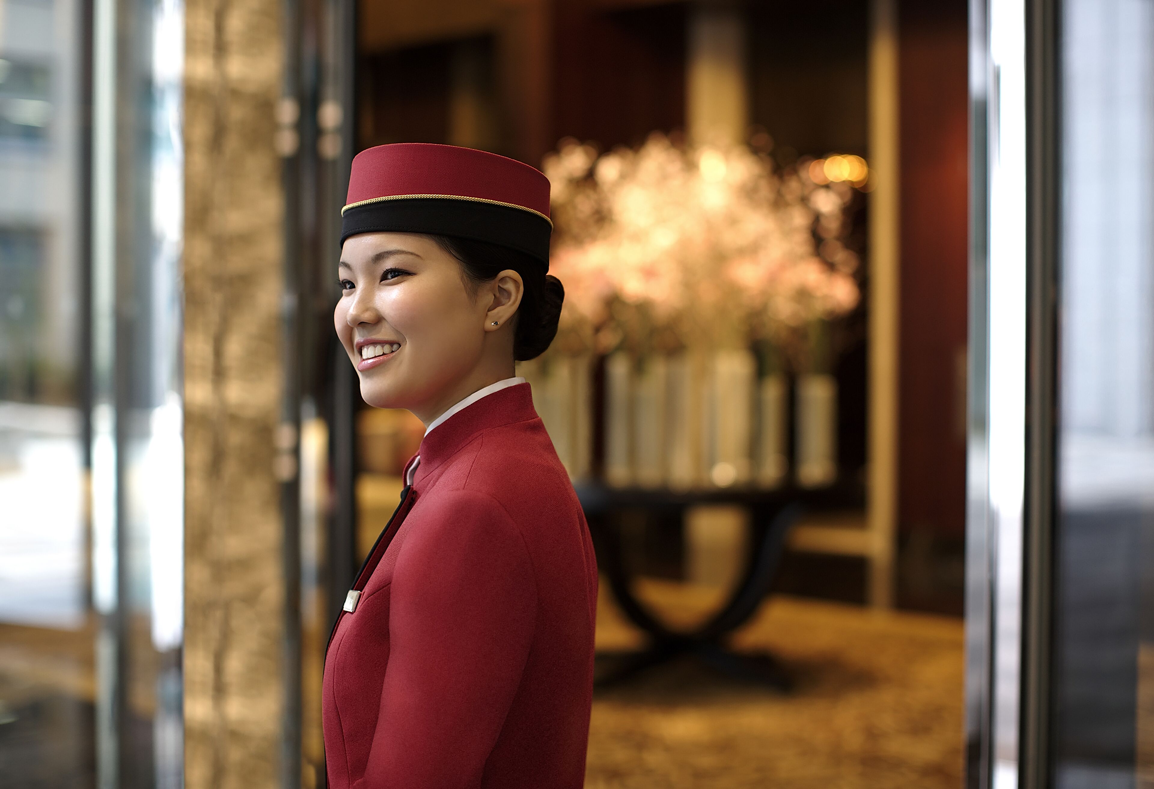 A person in a red uniform standing in front of a glass door with a blurred background.