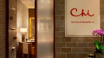 Ein Spa-Innenraum mit einer Rezeption, einem an der Wand befestigten Schild mit der Aufschrift "Chi The Spa at Shangri-La" und einer Wanddekoration mit einer Blumenkomposition.