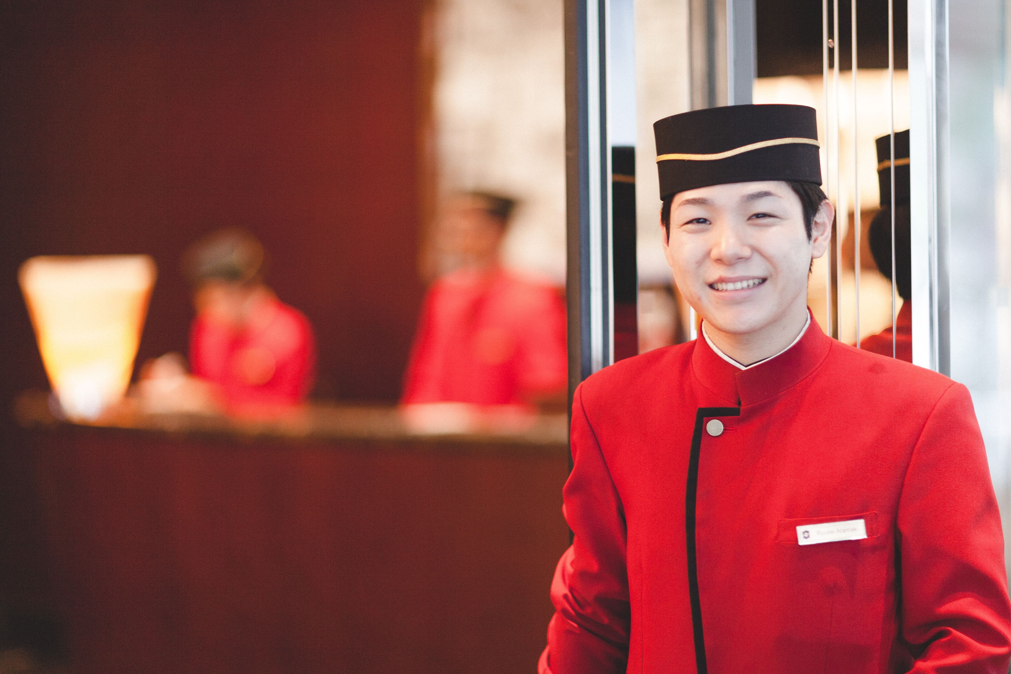 A hotel reception area with a staff member in a red uniform standing in front of a glass partition.