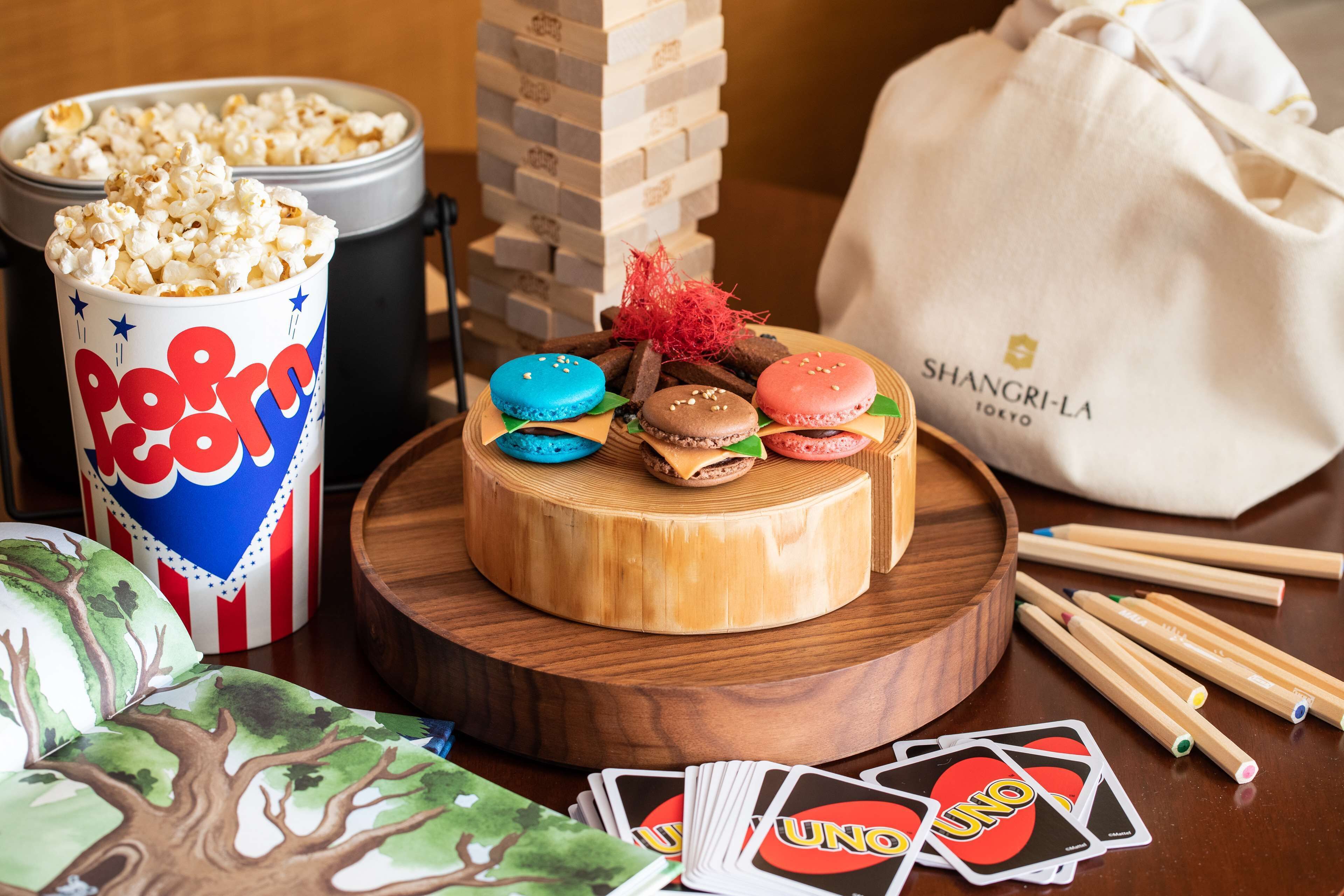 A wooden table with a cake, popcorn, UNO cards, and a Mahjong set.
