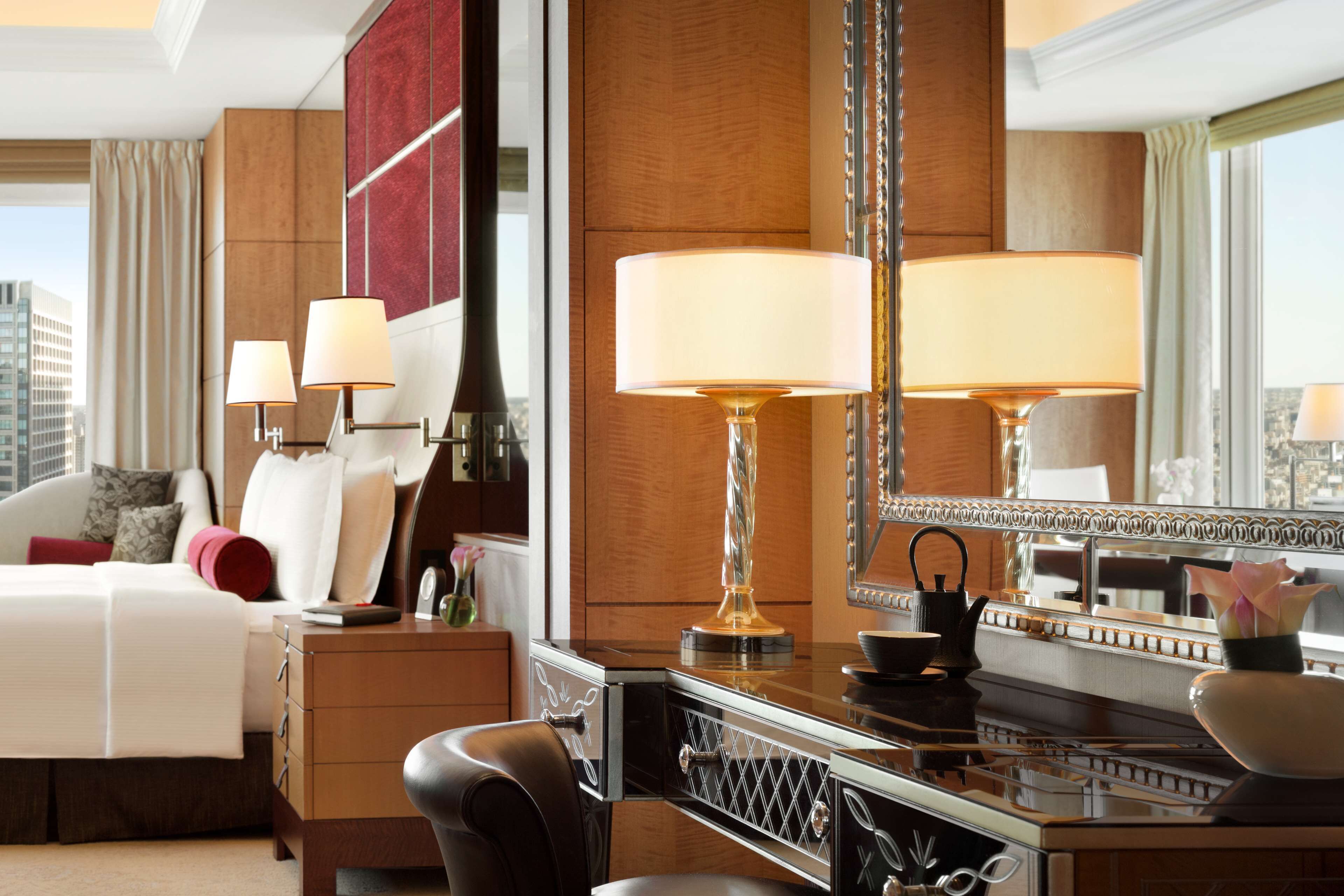 Et hotelværelse med en seng, sengeborde med lamper, et toiletbord med spejl og udsigt til byen.